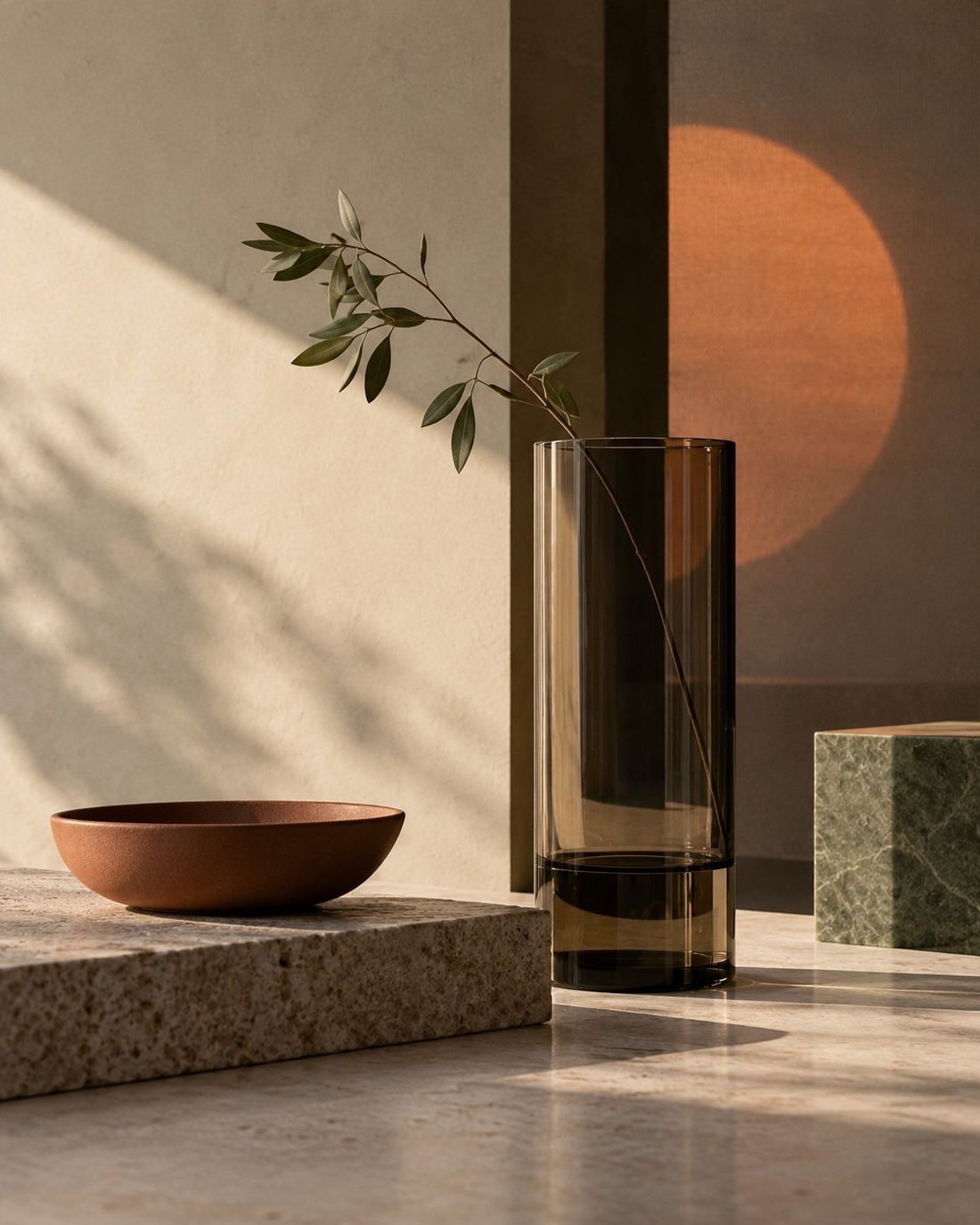 Warm low light across a stone ledge with a clay bowl and a glass vase